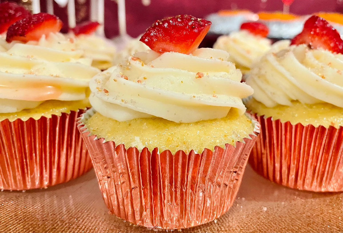 A strawberry shortcake cupcake in a foil case, topped with cream and a fresh strawberry