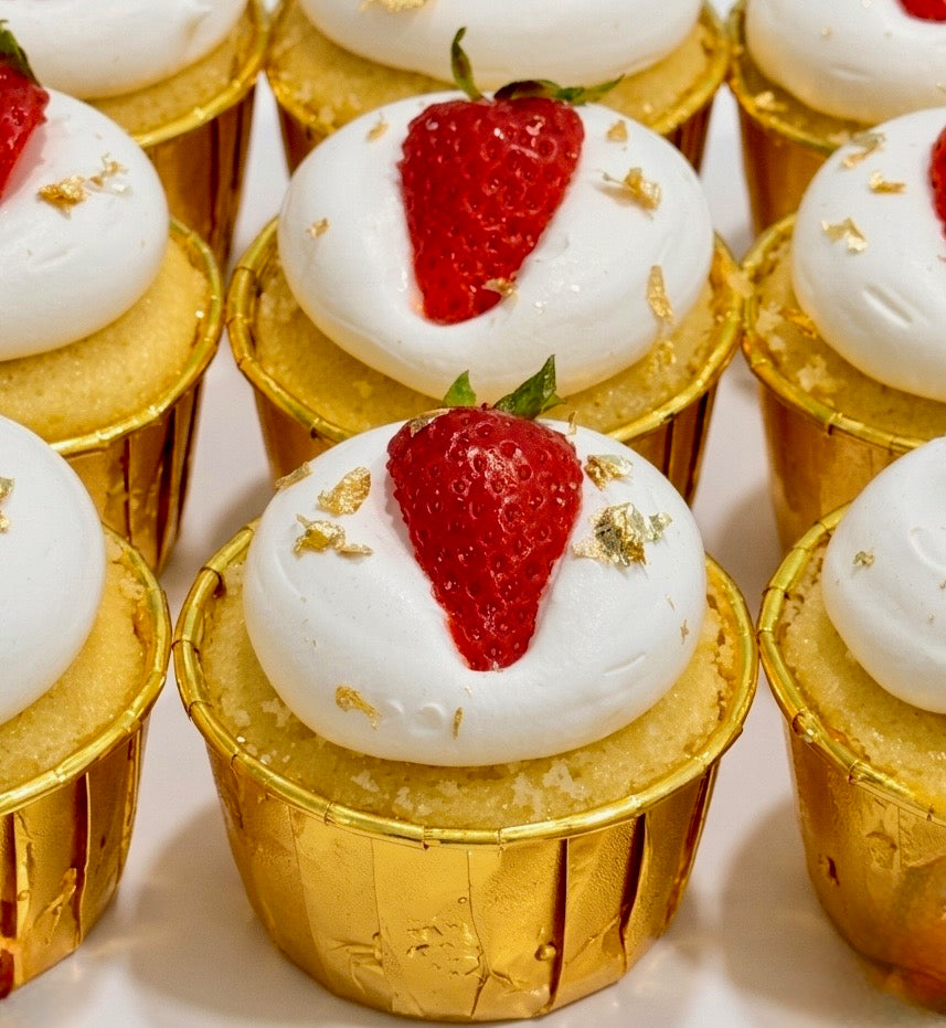 A strawberry shortcake cupcake in a foil case, topped with cream and a fresh strawberry